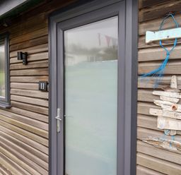 An exterior wooden wall with a frosted glass door and a small window beside it at Beside the Sea in Eype