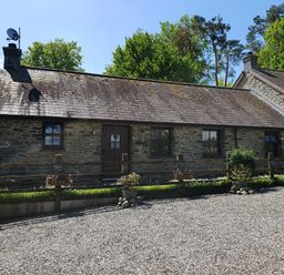 A stone cottage with wooden windows and a gravel driveway at Ty Barcud in Llanfair Clydogau