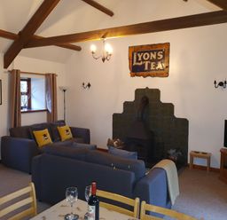 A living room with two sofas a wood stove a television and a dining table at Ty Barcud in Llanfair Clydogau