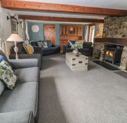 A living room with grey sofas a wooden coffee table a stone fireplace and wooden beams at Hazel Barn in North Molton