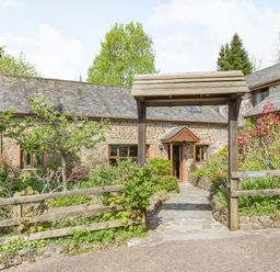 A stone cottage with a wooden archway and garden in front at Hazel Barn in North Molton