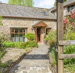 A stone cottage with a pathway and garden plants at Hazel Barn in North Molton