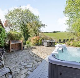 An outdoor patio with a hot tub stone flooring dining table and chairs and a brick barbecue at Hazel Barn in North Molton
