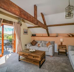 A living room with wooden beams two gray sofas a wooden coffee table and open French doors leading to an outdoor patio at Oak Cottage in North Molton