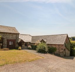 An exterior view of stone buildings with slate roofs surrounded by grass and bushes at Oak Cottage in North Molton