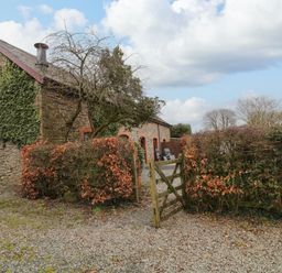 A stone house with ivy on the wall near a wooden gate and leafless trees at The Hawthorns in North Molton