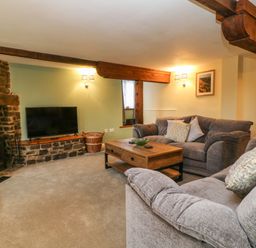 A living room with grey sofas a wooden coffee table a stone fireplace and a television at The Hawthorns in North Molton