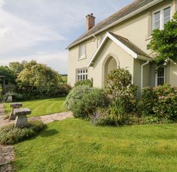 A front garden with a stone path shrubs and a house with a covered entrance at Crablake Farmhouse in Exminster