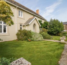 A garden with grass bushes stone benches and a house with white windows at Crablake Farmhouse in Exminster