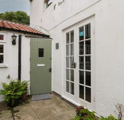 An outdoor corner with a green door a white double glass door potted plants and a small lantern light at The Nook in Whitby