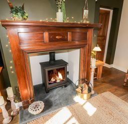 A living room with a wood burning stove in a wooden fireplace a bucket with firewood and candles at The Nook in Whitby