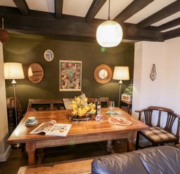 A dining room with a wooden table set with a magazine wine bottle cups and food with a bench and chairs against a green wall with lamps and mirrors at The Nook in Whitby