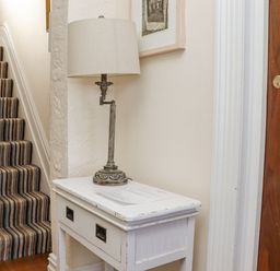 A striped carpeted staircase next to a white wooden side table with a lamp and papers on it at Heron in St Ives