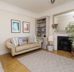 A living room with a beige sofa cushions a bookshelf a fireplace with a large mirror and a potted plant at Whistler in St Ives