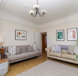 A living room with two sofas, cushions, framed artwork on walls, a side table with lamp, a patterned rug, and a plant at Whistler in St Ives