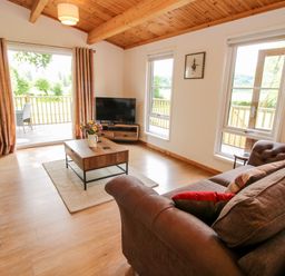 A living room with two sofas a coffee table a television and sliding doors leading to a balcony at The Log Cabin in Newnham Bridge near Tenbury Wells