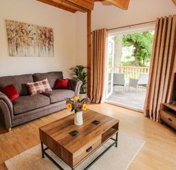 A living room with a sofa and coffee table opening onto a wooden balcony with chairs at The Log Cabin in Newnham Bridge near Tenbury Wells