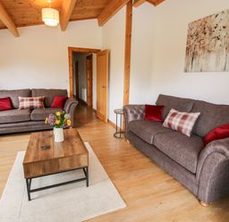 A living room with two brown sofas red and plaid cushions a wooden coffee table with flowers and wooden ceiling beams at The Log Cabin in Newnham Bridge near Tenbury Wells