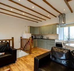 A kitchen and living area with black leather sofas wooden ceiling beams and green cabinets at Stable Cottage in Port Isaac