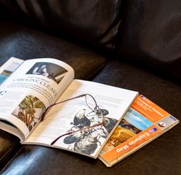 An open magazine and a folded map on a dark leather surface with a pair of glasses