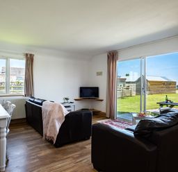 A living room with black leather sofas a small television and dining table with chairs at Atlantic Lodge in Port Isaac