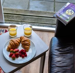 A small table with two croissants strawberries raspberries and two glasses of orange juice next to a leather chair with books on the armrest at Atlantic Lodge in Port Isaac