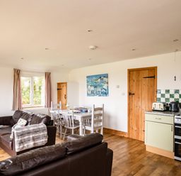 A living and dining area with two brown leather sofas a white dining table with chairs a kitchen corner with appliances and wooden doors at Campion Lodge in Port Isaac