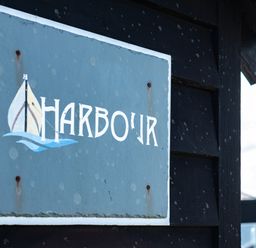 A sign with a sailboat and the word Harbour on a dark wooden wall at Harbour Lodge in Port Isaac
