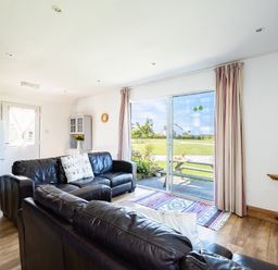A living room with leather sofas a sliding glass door leading to a garden and a television on a wall at Harbour Lodge in Port Isaac