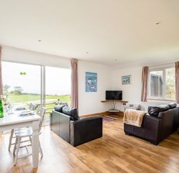 A living room with two leather sofas a television and a dining table near large sliding glass doors at Puffin Lodge in Port Isaac