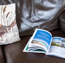 A brown leather sofa with a bird-printed cushion and an open magazine