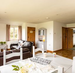 A living room with brown leather sofas a white dining table with colorful mugs and a map and a kitchen area at Dolphin Lodge in Port Isaac