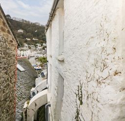 A view between two buildings showing rooftops and houses on a hillside with boats in a harbor at Spindrift in Polperro