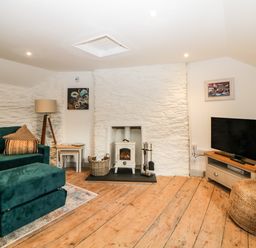 A living room with a green sofa and ottoman a floor lamp a wood stove a television on a stand and wooden floors at Spindrift Polperro