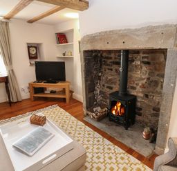 A living room with a stone fireplace and wood stove a tv on a wooden stand and a white tray on an ottoman at Cross View Cottage in Alston