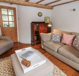 A living room with a beige sofa and patterned cushions a gray armchair a wooden cabinet and a white tray on an ottoman at Cross View Cottage in Alston