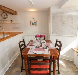 A dining area with a wooden table set with plates and glasses wooden chairs a kitchen counter with a sink and faucet and a large map on the wall at Cross View Cottage in Alston
