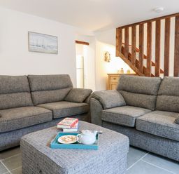 A living room with two grey sofas a grey ottoman with a tray of tea and biscuits and wooden stairs at Beach Road House in Hele Bay Ilfracombe
