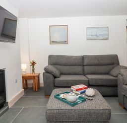 A living room with gray sofas a wall-mounted tv a fireplace and a wooden side table with a lamp at Beach Road House Hele Bay Ilfracombe