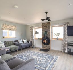 A living room with sofas a patterned rug a wall-mounted stove and a TV at Rynys in Llanddeiniolen near Llanrug