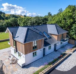 A two-story house with wooden paneling and tiled roof surrounded by trees and lawn at Rynys in Llanddeiniolen near Llanrug