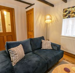 A living room with a blue sofa and striped cushions a wooden door a floor lamp and a window with patterned blinds at April Cottage in Whitby
