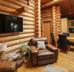 A living room with a leather armchair a glass side table with a lamp and plant a wall-mounted television and a dining table with four chairs at Brynallt Country Park Frankton near Ellesmere