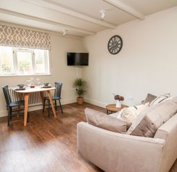 A dining table with two chairs near a window and a sofa with cushions in a living room at Llygad Y Dydd in Bow Street Wales