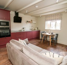 An open plan kitchen and living area with burgundy cabinets a dining table with two chairs and a beige sofa at Llygad Y Dydd in Bow Street Wales