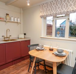 A kitchen with red cabinets a wooden table set for two and a window with patterned blinds at Llygad Y Dydd in Bow Street Wales