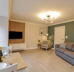 A living room with a gray sofa an armchair dining table with wine and glasses and a wall-mounted TV at Estuary Walk in Whitby
