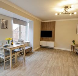 A living room with a dining table set near windows and a wall-mounted TV at Estuary Walk in Whitby