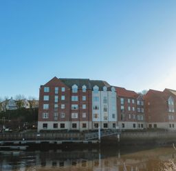 A row of brick and white residential buildings by a river with docks at Estuary Walk in Whitby