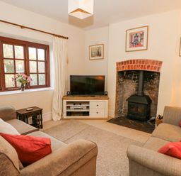 A living room with two sofas a television on a stand a wood burning stove and a window with curtains at Hillcrest in Oxwich near Port Eynon